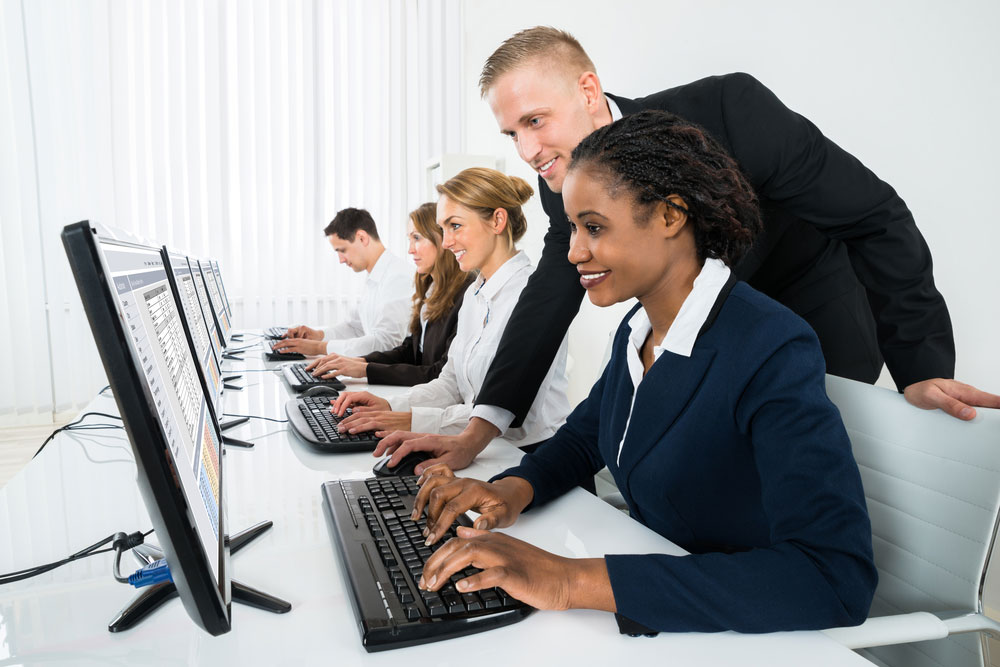 People sitting in front of computers with a trainer helping